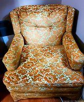 Front view of the vintage cushioned armchair showing the orange and white patterned upholstery, padded armrests, button-tufted backrest, and removable seat cushion.
