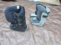 Two Biomet walking casts, black medium and gray extra small, displayed outdoors on tarp.