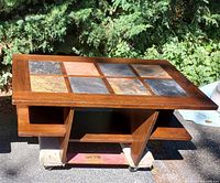 Full view of the rectangular wooden coffee table with slate inlaid top, showing the four side shelves and center shelf for storage. The slate tiles are various natural colors arranged in a grid pattern.