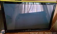 Front view of the Panasonic television screen with visible reflections and curtains in background, showing black bezel.