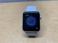 Apple Watch Series 3 42mm on a wooden surface showing the watch face with a blue swirling animation screen.