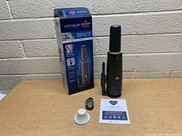 Photo of the boxed Bissell AeroSlim vacuum, handheld vacuum unit upright with brush attachment, a round white filter, a black brush cover, and a user manual on a wooden surface.