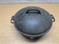 Top and side view of cast iron Dutch oven with lid on, showing domed lid and side handles.