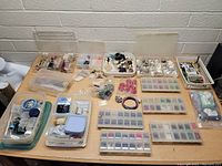 Wide view showing multiple trays and boxes of assorted jewelry and beads arranged on a table
