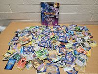 Photo showing a large assortment of Pokemon trading cards fanned out on a table with backs mostly showing, and the Pokemon Diamond Pearl scenario guide book behind.