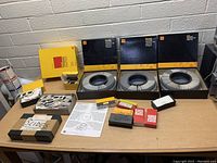 Photo of three Kodak Carousel Transvue 140 slide trays, each loaded with slides and boxed, with multiple smaller boxes of photographic slides and instruction papers on table.