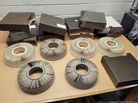 Overview photo showing seven circular carousel trays with vintage photographic slides and multiple dark cardboard storage boxes on a table.