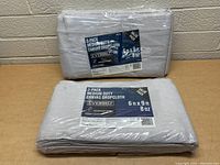 Two sealed 2-pack canvas drop cloths stacked and wrapped in plastic with visible Everbilt branding and dimensions 6x9 ft at 8 oz weight.