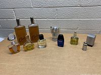 Full view of all nine assorted cologne bottles, arranged in a line on a wooden surface against a brick wall background.