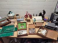 Wide view of assorted vintage items on table including ceramic vase, boxed items, vintage plaques, model tricycle, and electronics.