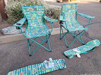 Pair of folding camping chairs with taco and avocado print fabric and turquoise frames, both unfolded outdoors on pavement, showing seats, armrests, and cup holders.