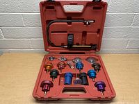 Full view of radiator pressure tester set in red carrying case, showing pressure pump and multiple radiator cap adapters.