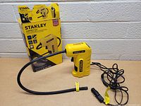 Full view of the Stanley Air Pro 120 air compressor with its box, showing the yellow body, attached hose with nozzle, and power cord.