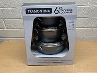 Front view of boxed set showing the stackable cookware through the window, listing included pieces and features.