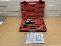 Full view of cylinder leakage tester kit in red carrying case, showing all components and manual.
