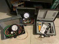 Photo of two grey plastic toolboxes each containing pressure meters with hoses and fittings alongside the UEI analyzer case