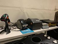 Photo of the lot items on white table including Tera barcode reader on stand, Dymo LabelWriter 460 Turbo wireless printer with guide, Zebra label printer, SPS Medical incubator, BK Precision multimeter.