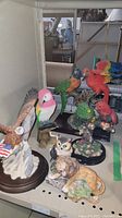 Group photo showing eagle, multiple colorful parrots, great horned owl, and African lion figurines on shelf