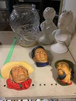 Bosson figure heads (Rawhide, Boatman, unnamed) and two white glazed children busts with glass jar shaped as a woman's head on a shelf