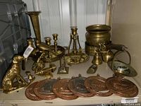 Overview of brass items including candleholders, a sitting animal figurine, pots, and decorative medallions spread on a surface.