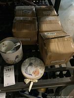 Six cardboard boxes containing the cat mugs, a cat mug with lid and spoon outside showing cat designs, lot tag included.