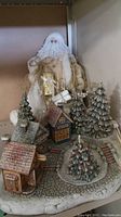 Full view of ceramic Christmas village with Santa figurine showing village houses, Christmas trees, and Santa dressed in white and gold.