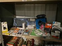 Shelf showing multiple unopened electronic accessories including Logitech keyboard box, mice, cables, and chargers arranged neatly.