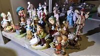 Wide view of multiple assorted figurines including Hummel children, Precious Moments, and Boyds Bears on a table