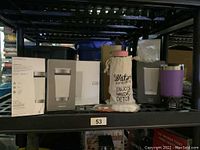 Shelved new insulated beverage bottles in their boxes including 4 stainless steel tumblers and one glass bottle with fabric sleeve.