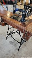 Full view of the Raymond Model 703 sewing machine mounted in the wooden sewing table with five drawers and ornate metal legs.