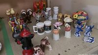 Photo showing multiple salt and pepper shaker sets arranged on a surface, showcasing a variety of animal and object designs including a fire hydrant, dogs, and mice with big ears.