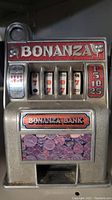 Front view of the Bonanza slot machine toy showing the Bonanza Bank signage, coin slot, and rotating reels with classic slot symbols.