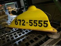 Side view showing yellow dome light with phone number 672-5555 in black text, base, and mounting mechanism.