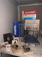 Photo showing bridge card deck, wooden architectural blocks box, three tin types on wooden blocks, multiple journals in different covers, and boxed board games stacked on shelf.