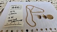 Chain and earrings laid out on paper with label noting 10k chain and 9k garnet earrings