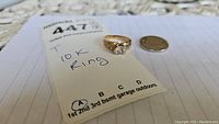 Ring on paper with tag and nickel coin for scale