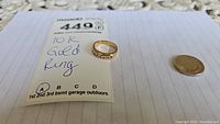 Ring placed on paper with MaxSold tag and nickel for scale