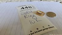 Front view of gold ring on inspection sheet with nickel for scale
