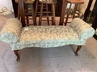 Front view of upholstered bench showing patterned fabric and wooden cabriole legs.