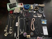 Photo showing a wide assortment of costume jewelry laid out, including necklaces, bracelets, rings, earrings, pins, and small accessories.