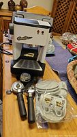 Full view of Faema Mistral Euro Star espresso maker with two portafilters and group head basket on front beside packaged espresso cups and saucers.