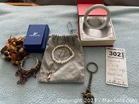 Lot laid out on cloth, including garnet chip earrings, pearl bracelets, Swarovski necklace with pendant in blue box, multicolor bead and stone necklace, and grey bangle bracelet. Seller note visible.
