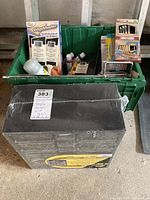 Green bin filled with assorted household items including paintbrushes, light bulbs, Edgemaster self-guided edger kit, paint stirrer, and metal vent cover placed in front of the bin.