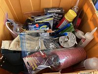 Photo of orange bin filled with various tools and accessories including coiled red nylon air hose, yellow spray can, packaged tools and caulking tubes.