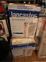 Two stacked original boxes of Lancaster oil-filled heaters, both labelled 700W with thermostat and compact design details, showing some wear and tear.
