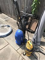 Blue Simoniz electric pressure washer model S1600 standing on patio next to yellow Active Products unit and coiled hose.