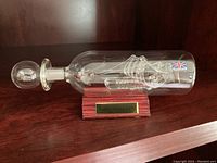 Side view showing glass ship in bottle on wooden stand with plaque 'Santa Maria 1492'