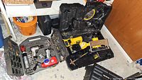 Two carrying cases on a table, one open with Dewalt cordless reciprocating saw, circular saw, battery, and charger; the other metal case with pneumatic tools.