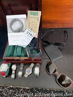 Overview of wooden watch box, six watches, packaged smart bracelet, two pairs of sunglasses, and accessories