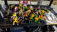 Full lot of approx 27 assorted action figures including Teenage Mutant Ninja Turtles, Dick Tracy, General Traag and others arranged on black rack.